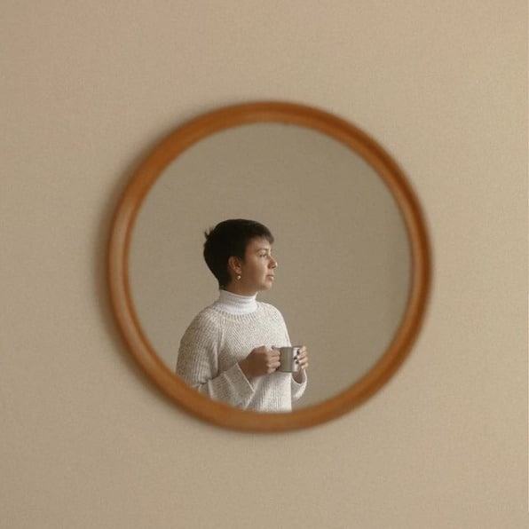 Espelho em parede, refletindo a imagem de Lua Couto segurando uma caneca de chá