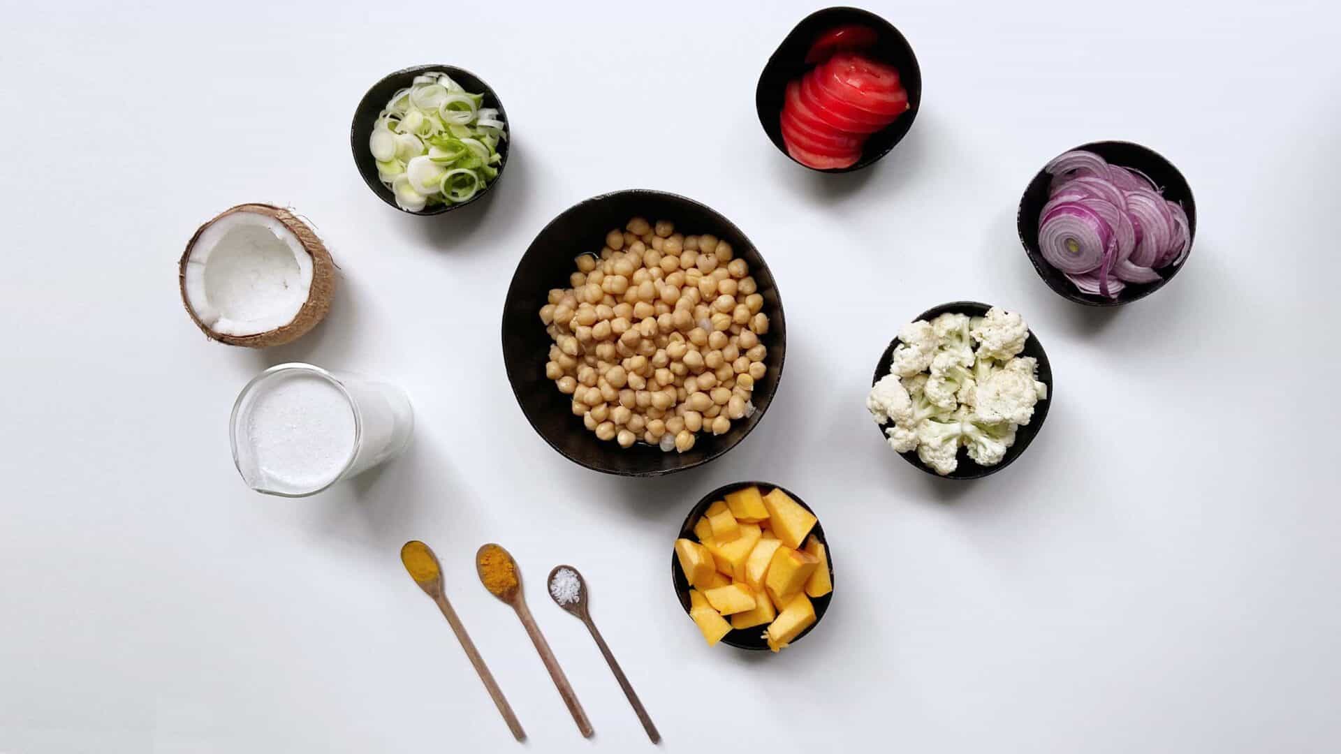 Ingredientes para receita com grão de bico, especiarias e vegetais, todos em potes sobre fundo branco