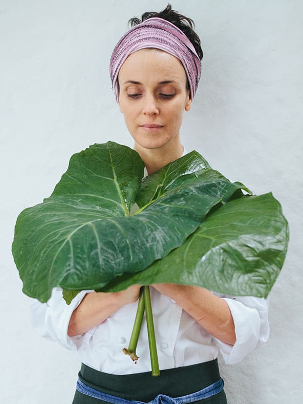 A chef Helena Rizzo posa com folhas de taioba, uma PANC (Planta Alimentícia Não Convencional)