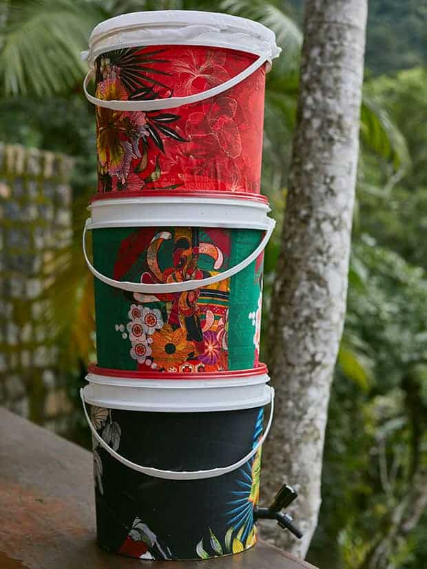 Composteira caseira customizada com tecidos estampados, apoiada em parapeito de madeira. AO fundo, paisagem de serra.