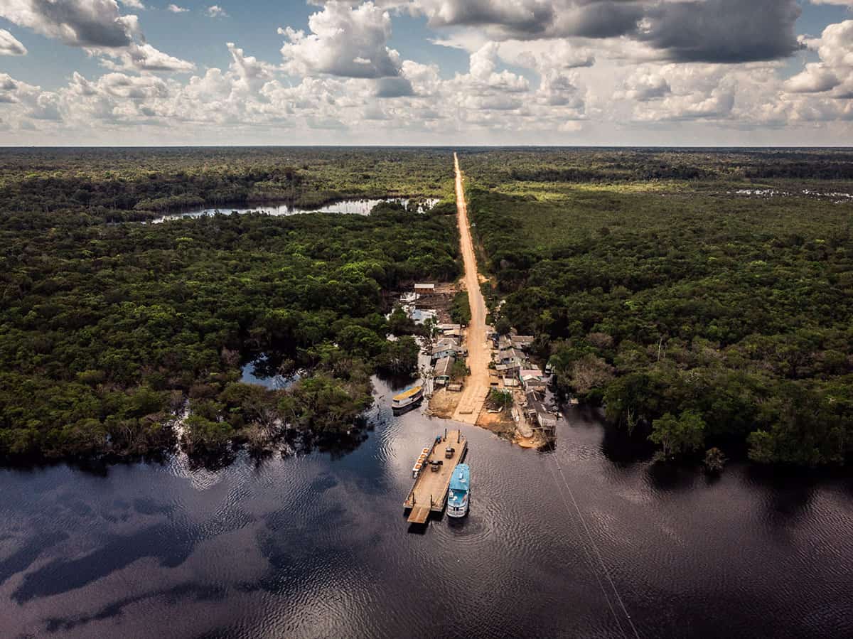 Vista aérea da BR 319, ainda em construção, cortando vilarejo na Amazônia