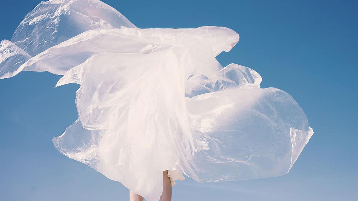 Mulher envolvida em plástico, como um vestido plástico voando com o vento para falar de roupas e poluição