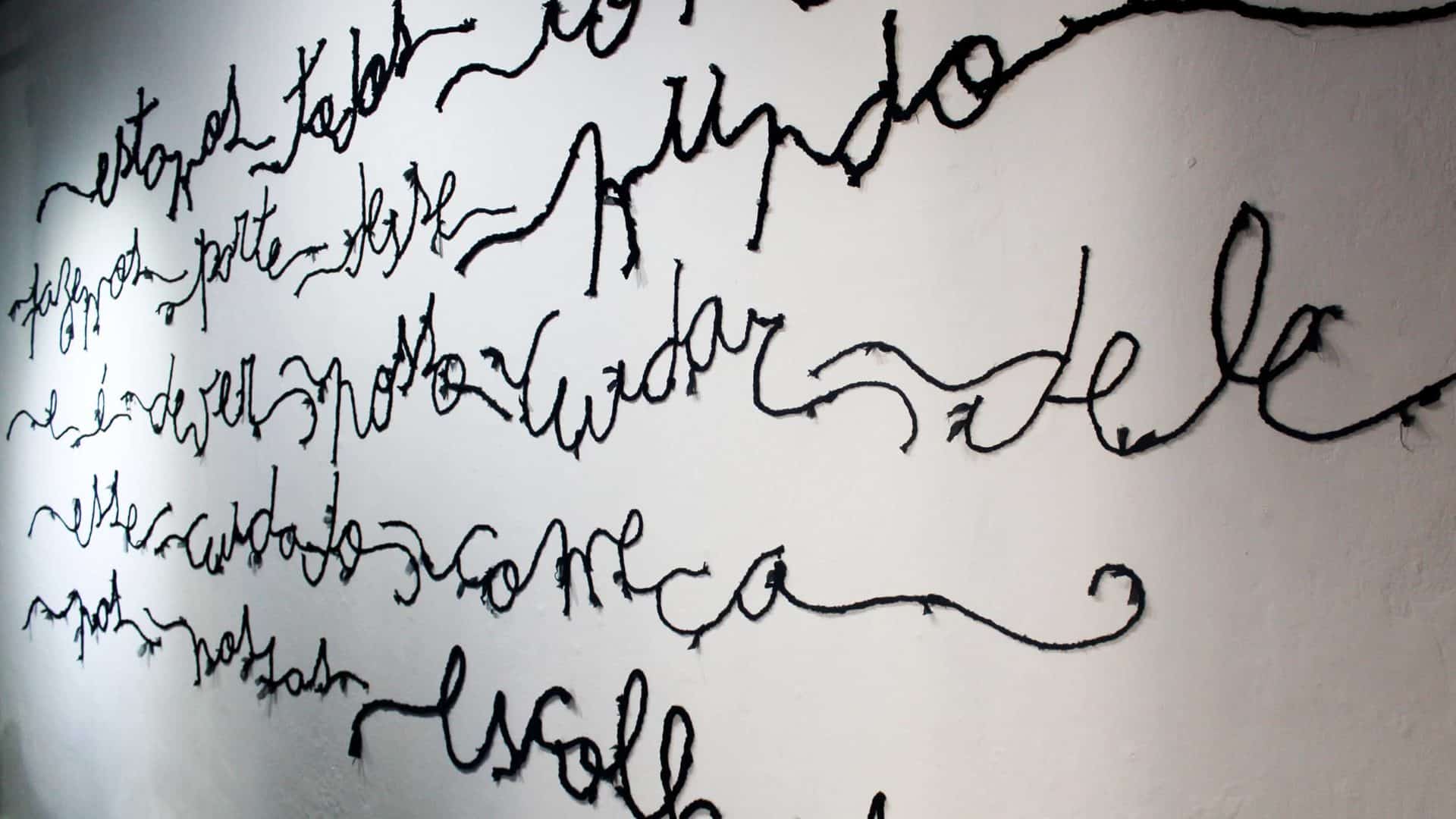 Poesia bordada, aplicada em parede, em exposição do estilista e poeta Teko Semente