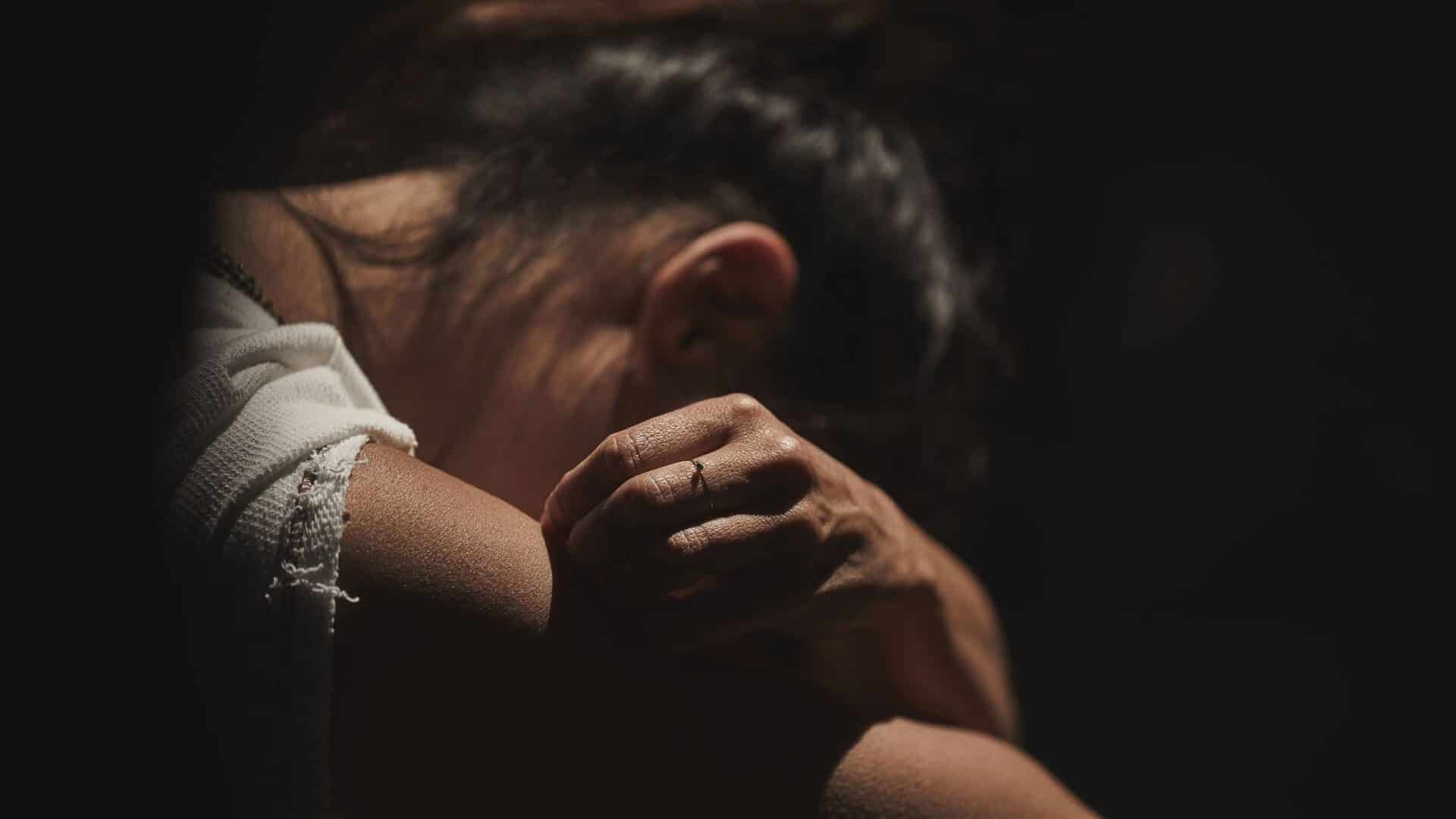 Mulher agachada com o rosto coberto pelos braços